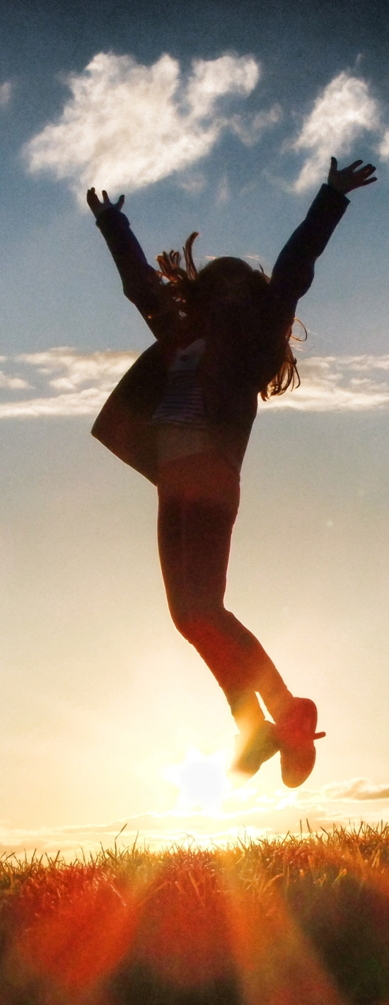 Auringonvaloa vasten kuvattu henkilö hyppää ylöspäin kädet ojennettuina.